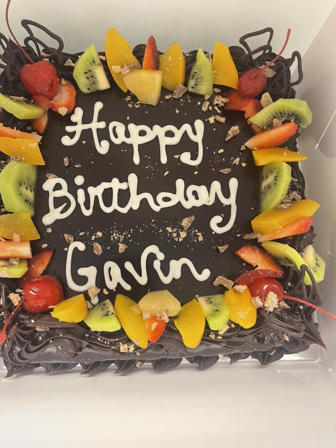 Chocolate-glazed birthday cake decorated with kiwi, peach, strawberry and cherries