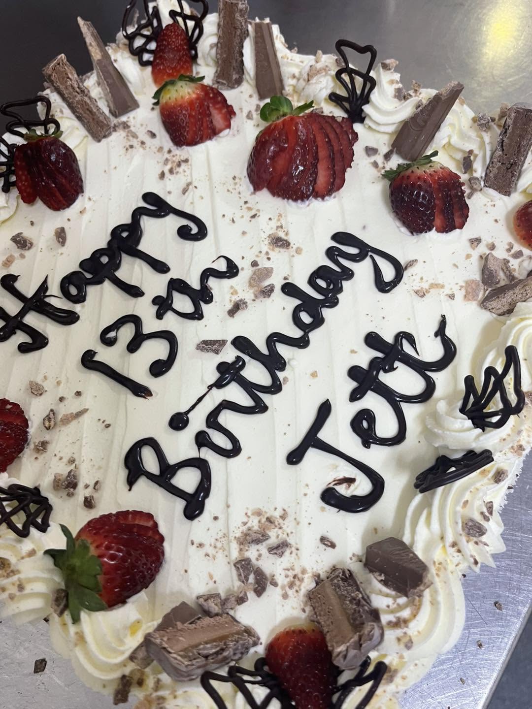 Cream-topped celebration cake with strawberries, chocolate pieces and piped chocolate