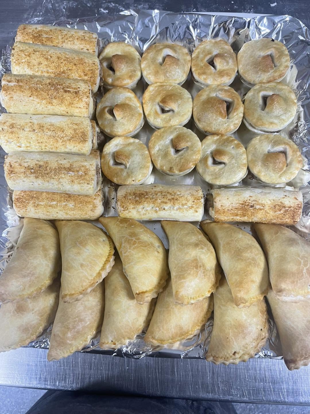 Tray of golden sausage rolls, mini pies and pasties on foil